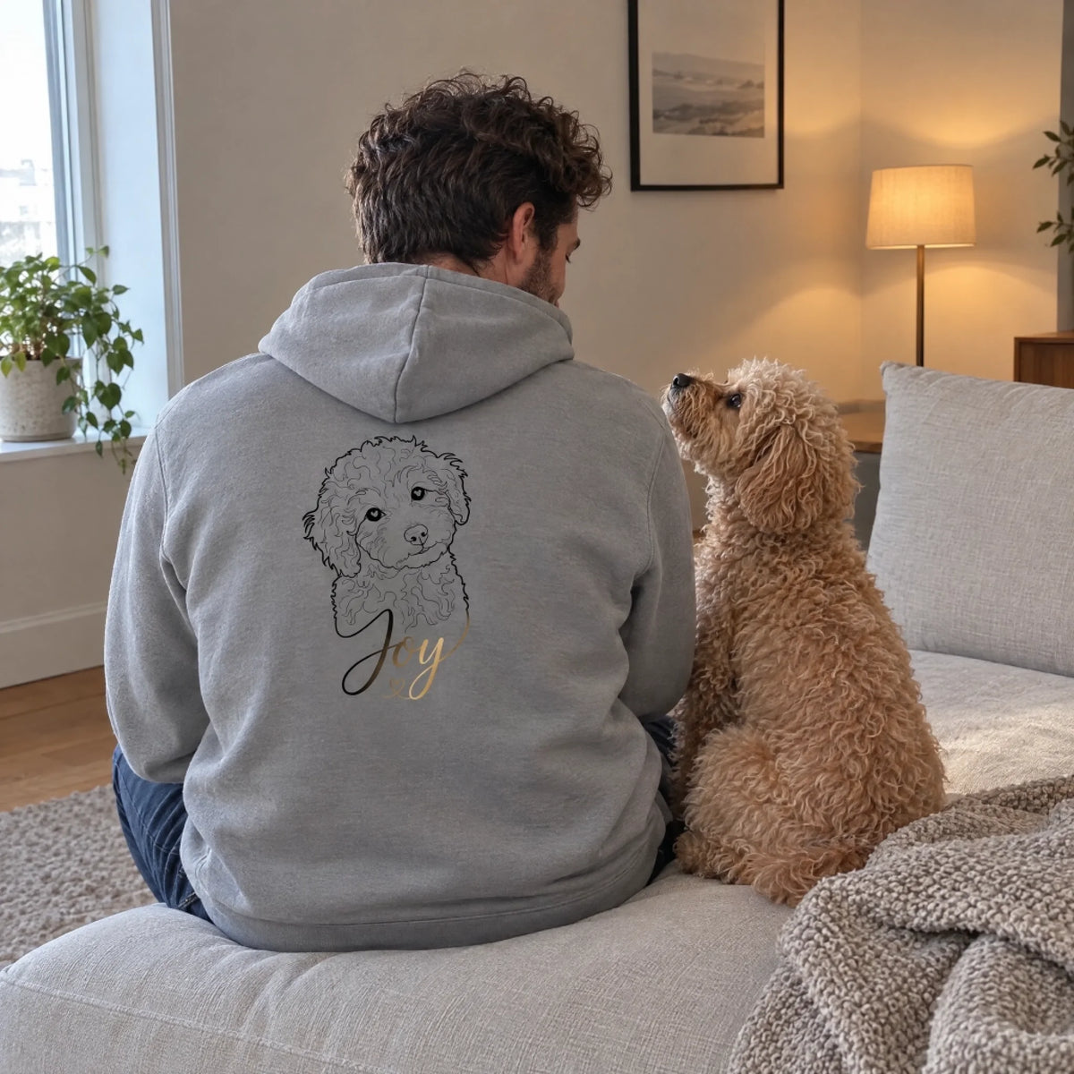Mann im grauen Hoodie mit Line-Art vom Pudel Joy auf dem Sofa neben seinem Hund