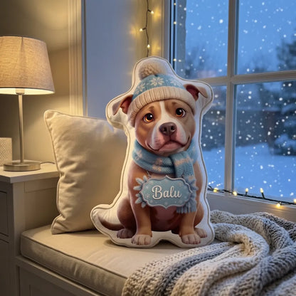 Kissen in Hundeform mit Strickmütze und Schal auf der Fensterbank, draußen fällt Schnee